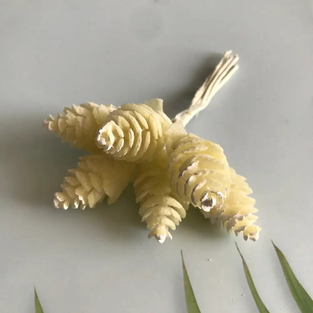 A cluster of pale yellow intricately textured artificial pinecones tied with white string in an artificial flower wreath
