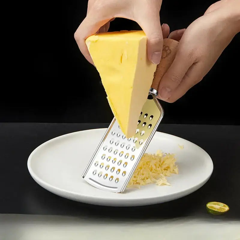 A stainless steel 3-in-1 multifunctional grater with a wooden paw print handle grating yellow cheese