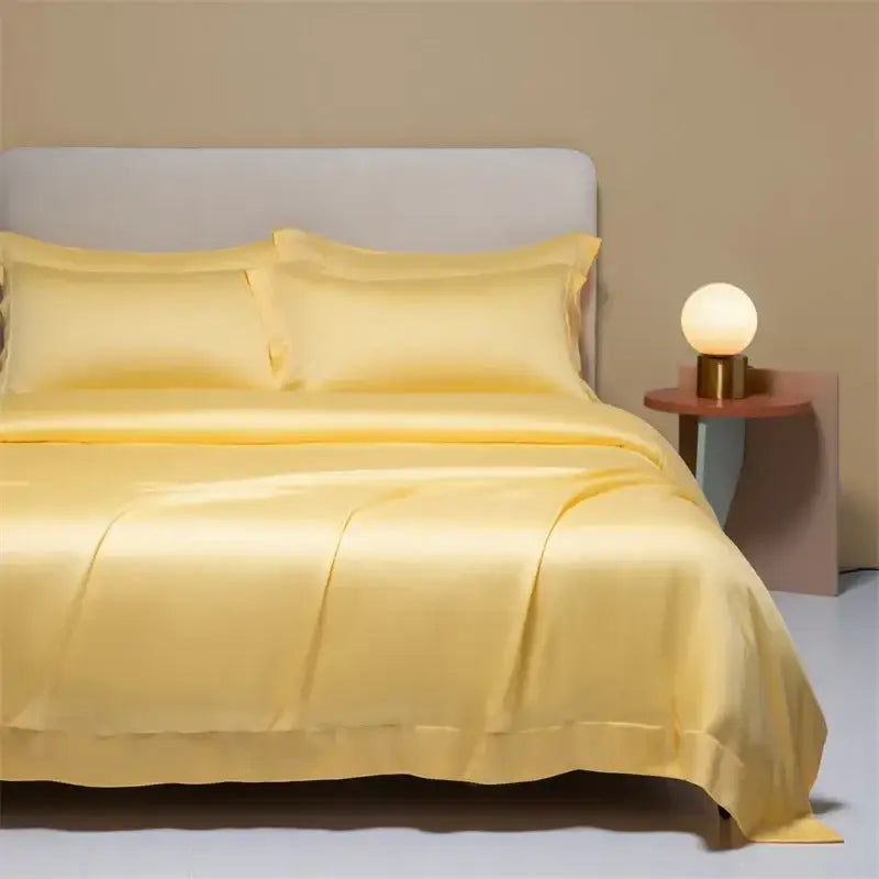 A luxurious golden-yellow peach satin cooling cotton solid bedding set with duvet and pillows draped over the mattress