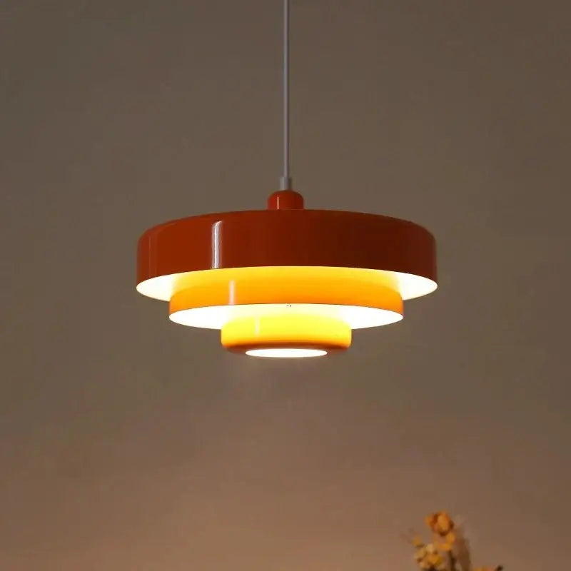A modern bauhaus style pendant lighting with glossy orange outer ring and warm yellow inner rings on metallic rod