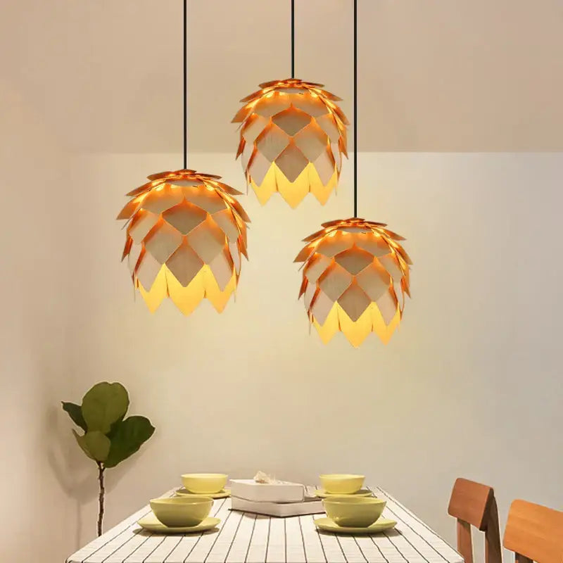 Three golden pinecone wooden style orange and gold pendant lights with layered leaf segments hang above dining table decorbites handmade smart