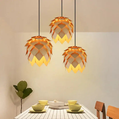 Three golden pinecone wooden style orange and gold pendant lights with layered leaf segments hang above dining table decorbites handmade smart