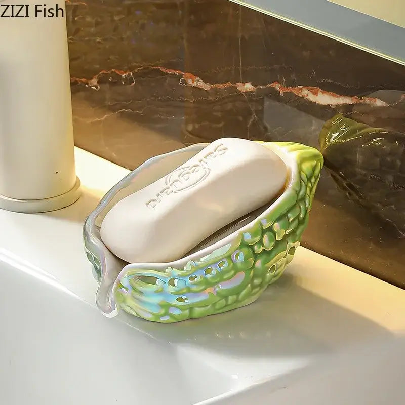 A green glossy seashell soap dish with blue and silver accents holding a white soap bar for bitter gourd ceramic use
