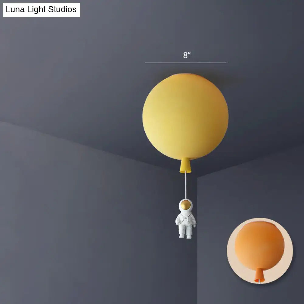 Yellow balloon-shaped acrylic pendant light with a small astronaut figurine hanging below astronaut ceiling lamp