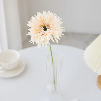 A delicate cream-colored artificial gerbera with layered petals in a clear glass brushed gerbera vase for living room decor