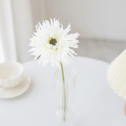 A delicate white artificial flower with feathery petals in a clear glass pink brushed gerbera vase for living room decor