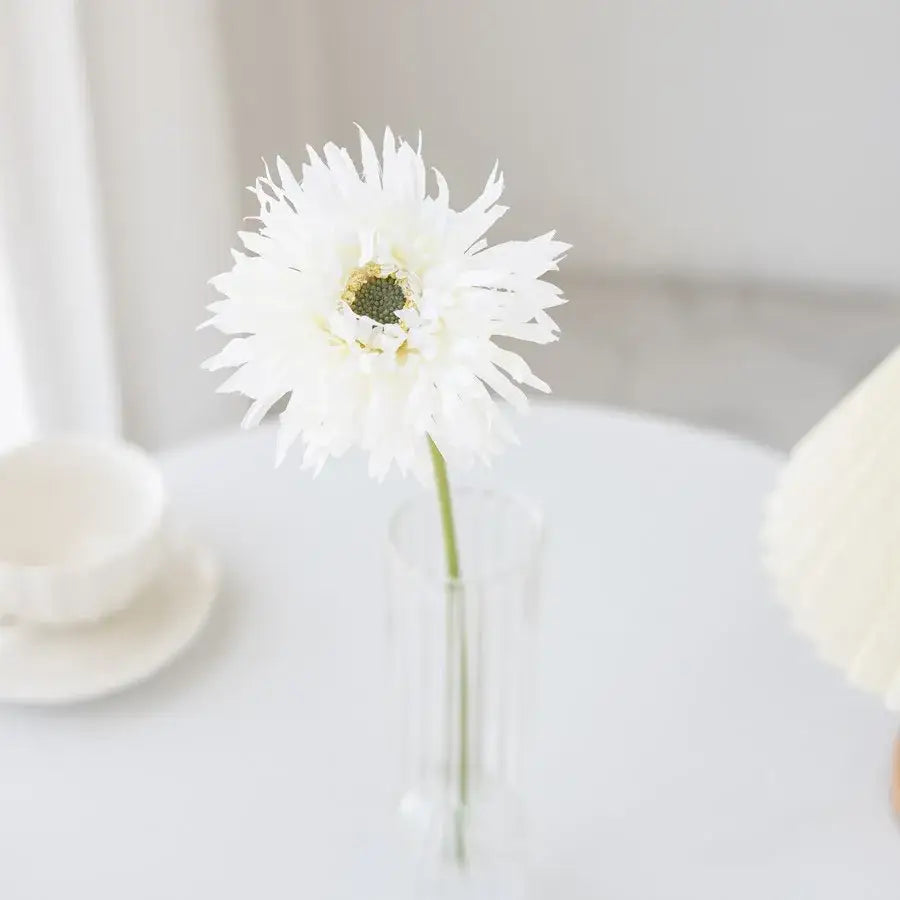 A delicate white artificial flower with feathery petals in a clear glass pink brushed gerbera vase for living room decor