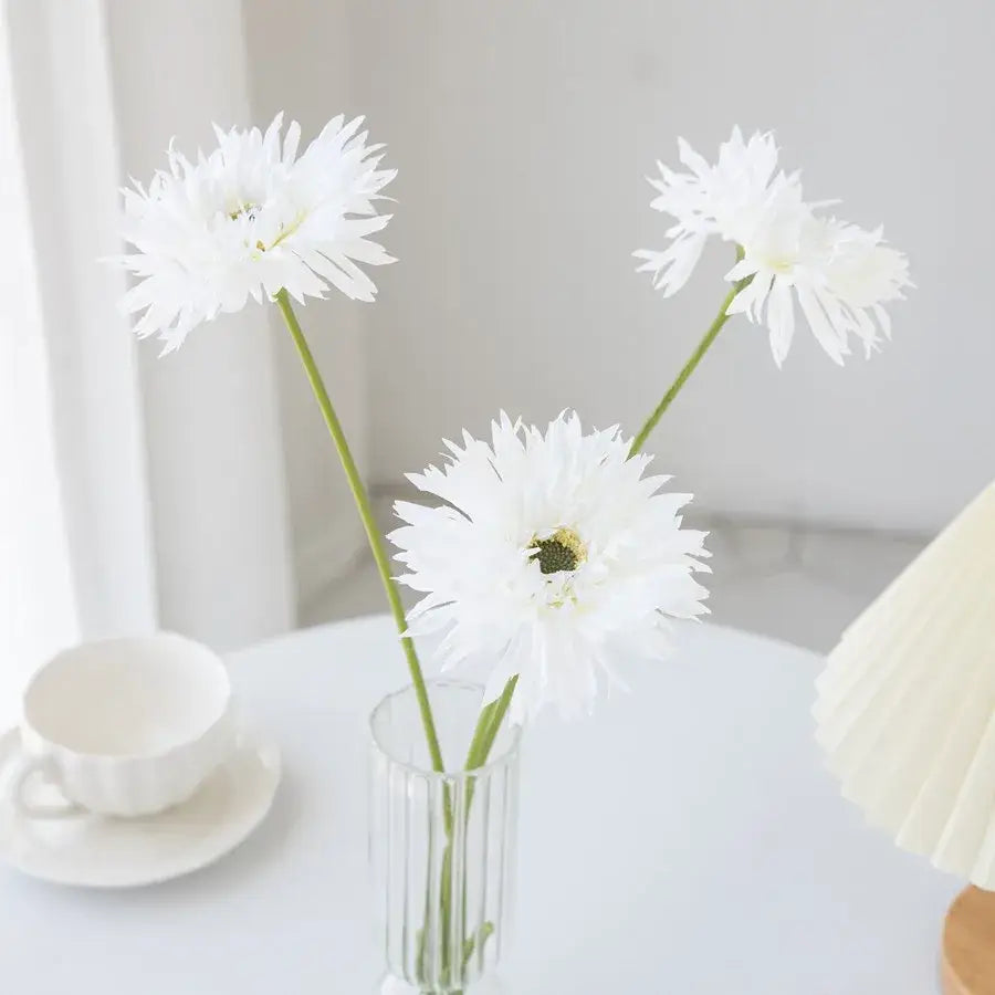 Three white artificial daisies in a clear glass pink brushed gerbera vase with vertical ridges for living room decor