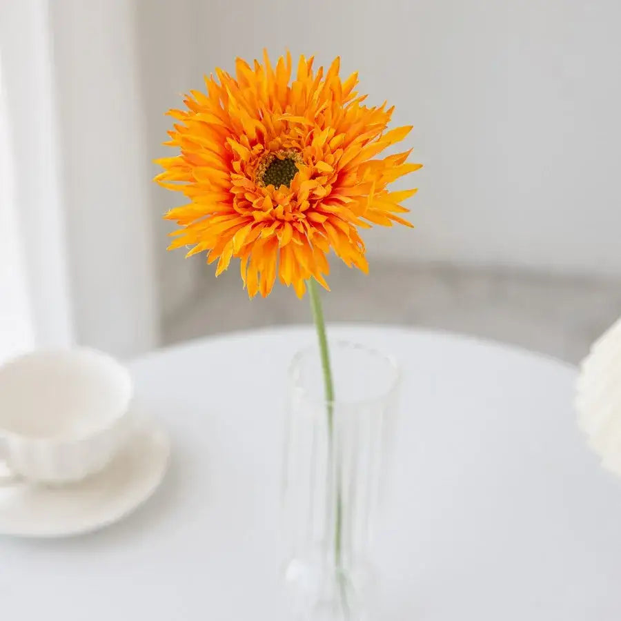 A vibrant orange artificial gerbera in a clear glass brushed gerbera vase for living room floral decor