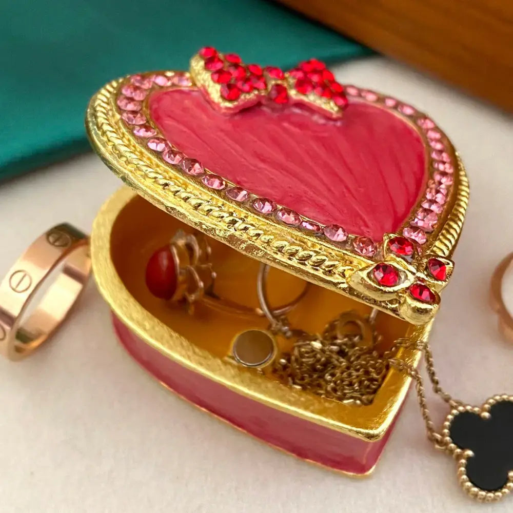 A vibrant pink and gold heart-shaped jewelry trinket box with rhinestones and a red bow storage case