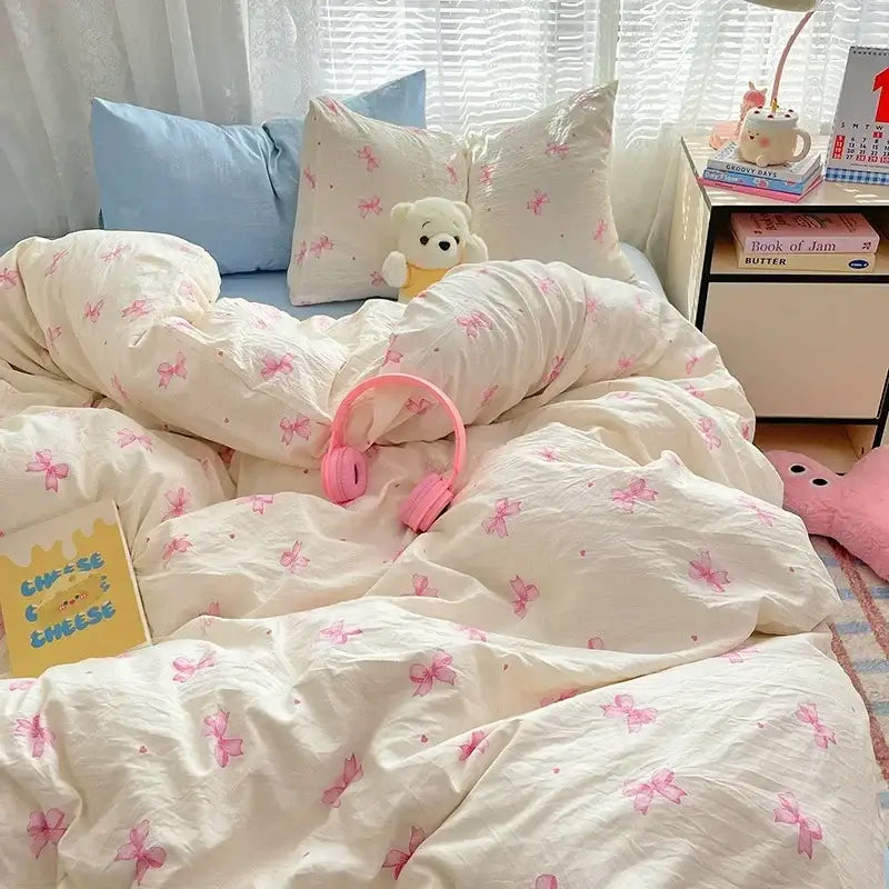 Pink over-ear headphones rest on a cream comforter set with pink bow patterns from decorbites cozy cartoon printed collection