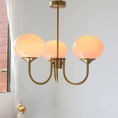 Brass-finished pendant lights with three warm-toned pink glass globes for decorbites designer loft bedroom decor