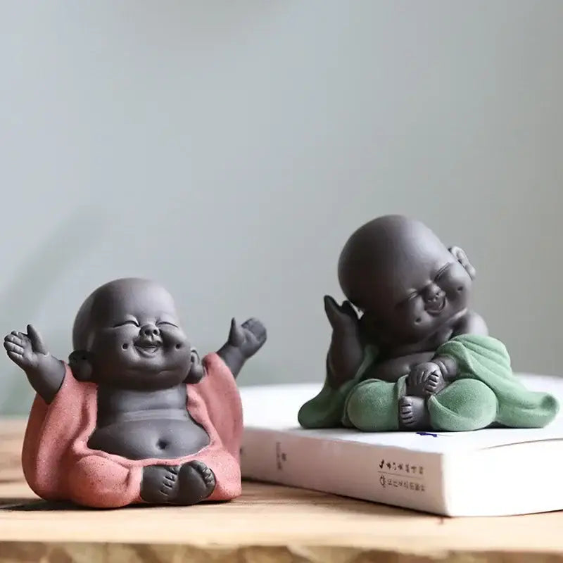 Two ceramic maitreya buddha statue tea sculptures in pink and green robes with smooth matte finishes for living room decor