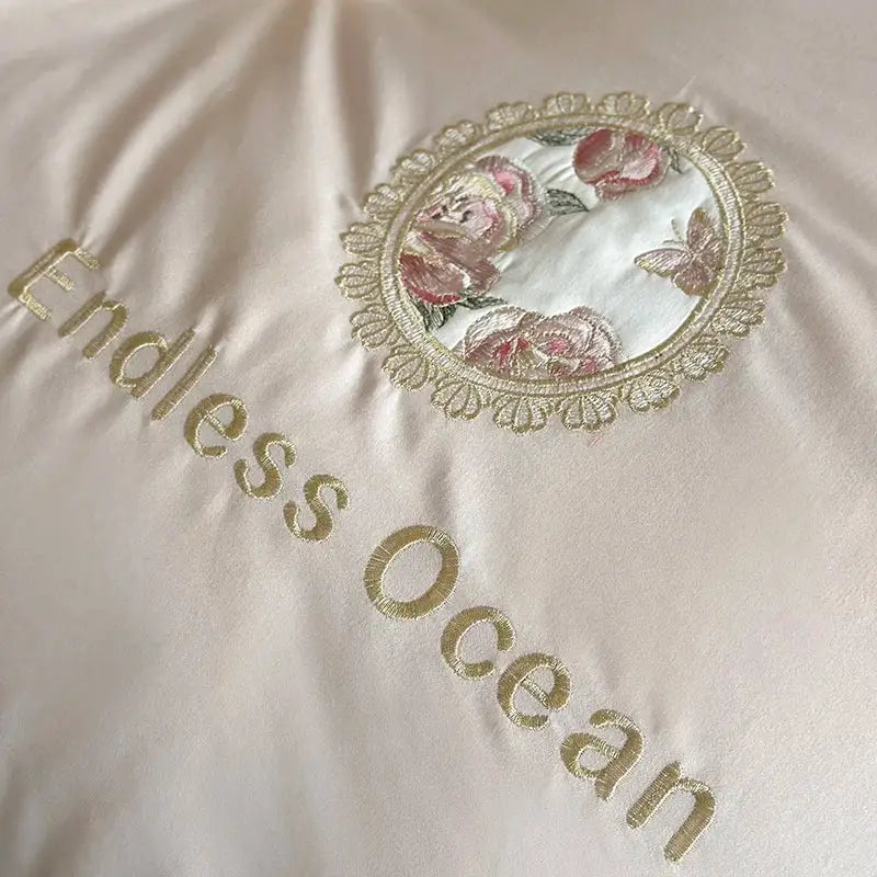 Cream-colored egyptian cotton bedding set with pink purple flowers embroidery and golden lace framing endless ocean text