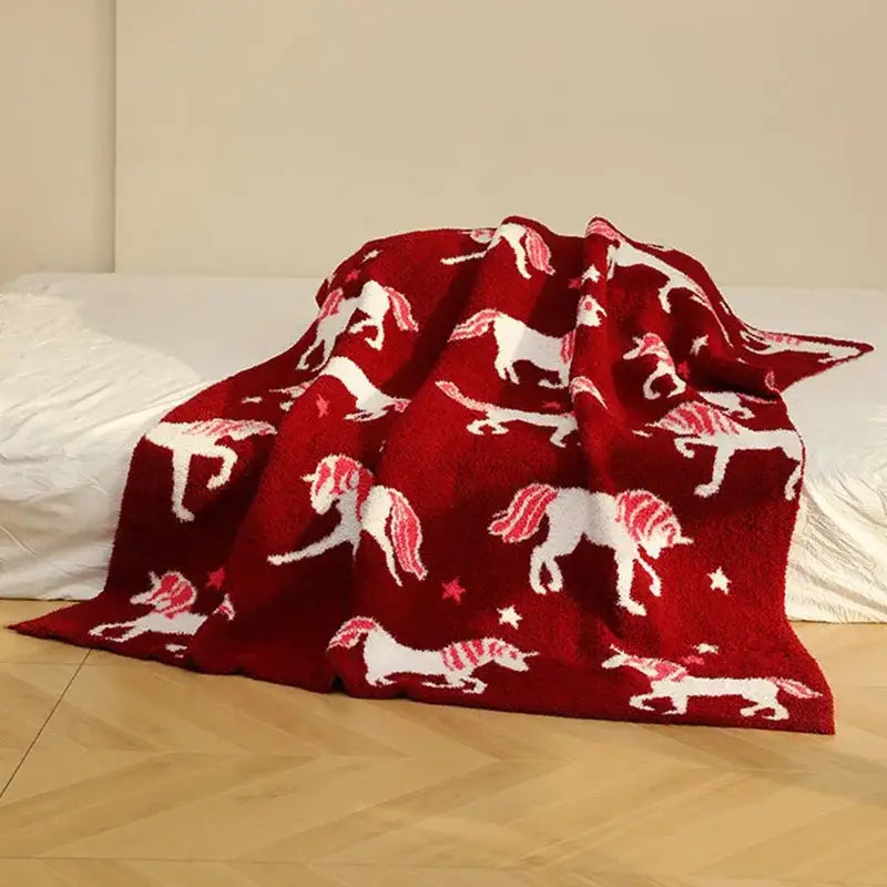 Plush red unicorn blanket made of fleece red material featuring white unicorns with pink manes and star patterns