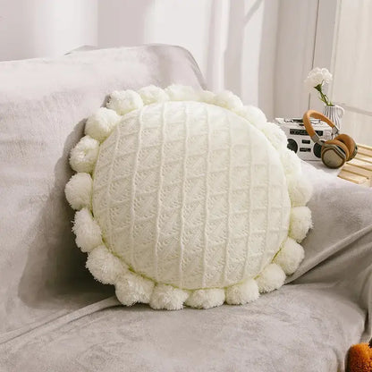 Cream-colored round pillow with textured knit center and pom-pom trim for plush white and soft pink flowers pillows home decor