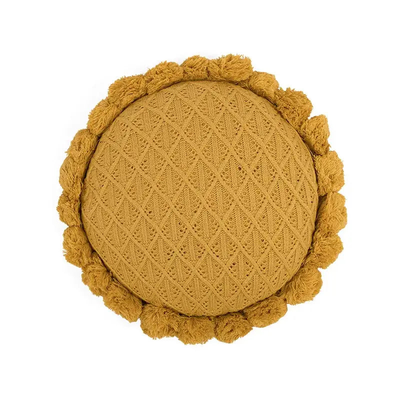 A round mustard-yellow knit cushion with diamond texture and pom-pom trim for home decor or decorbites 3d flowers pillows