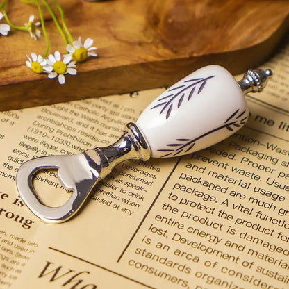 White ceramic beer bottle opener with silver accents and leaf pattern resting on an open book for kitchen use