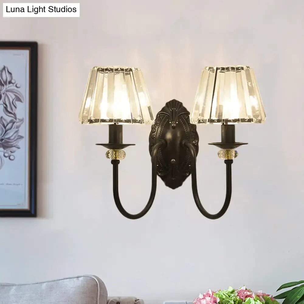 Antique bronze two-light wall sconce with black metal frame and clear crystal shade for bedroom use