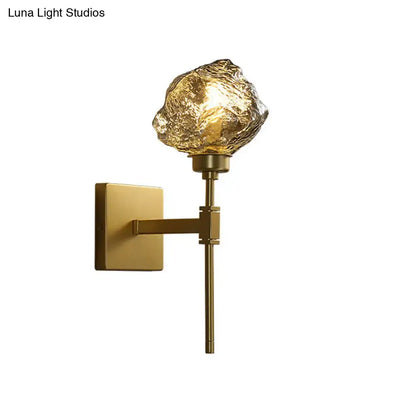 Gold-toned post modern brass wall light sconce with textured amber glass shade shaped like an irregular rock for living room