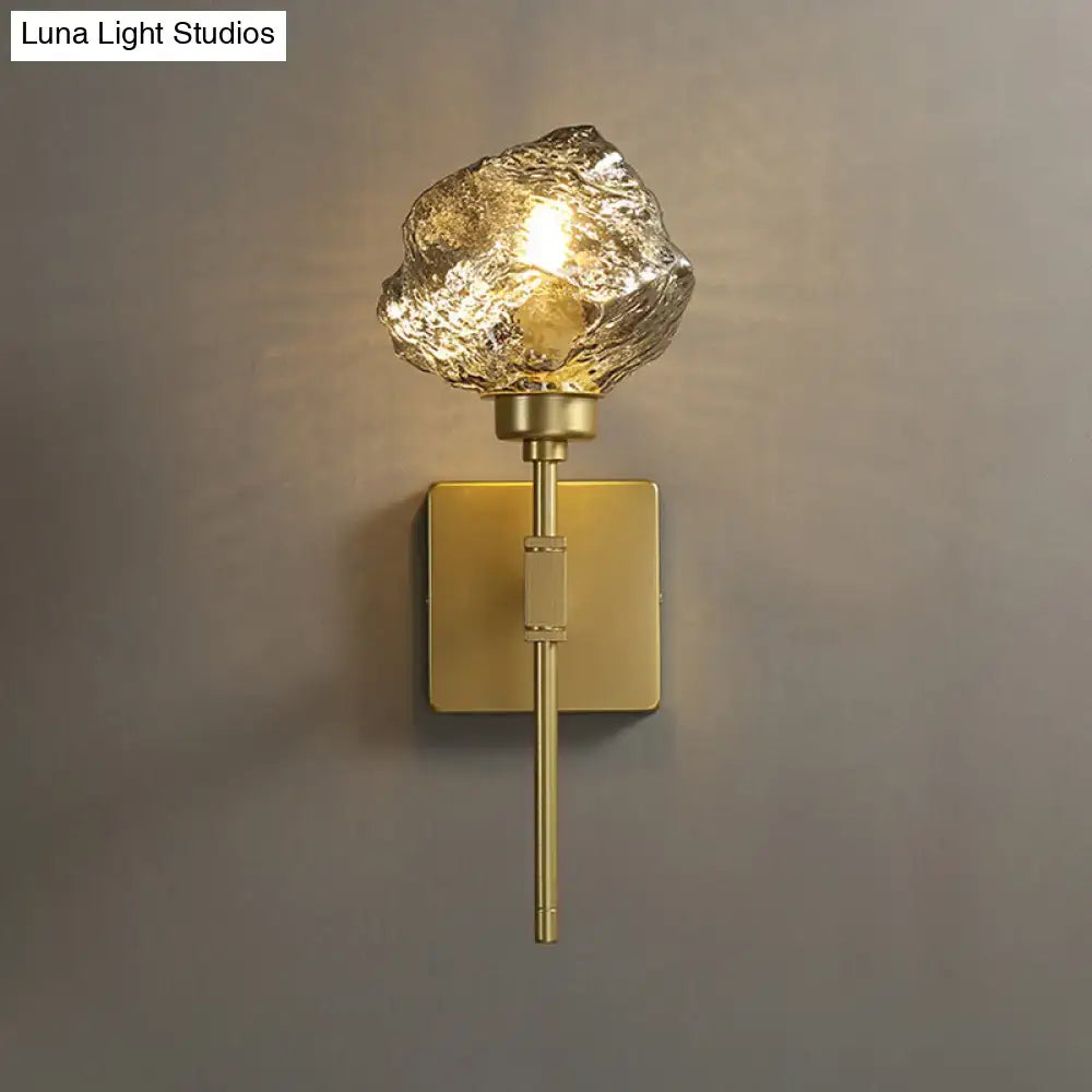Post modern brass wall light sconce with amber textured glass shade shaped like an irregular rock for living room