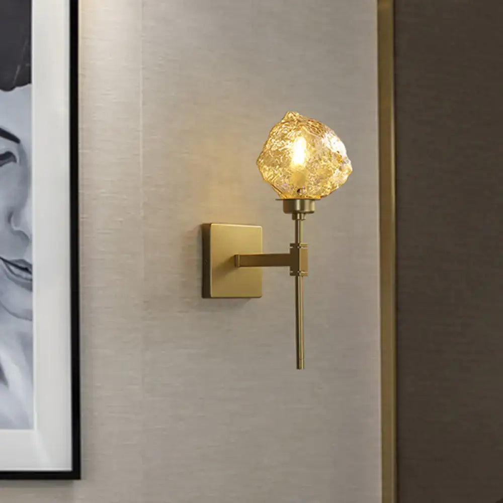 Post modern brass wall light sconce with a gold-toned textured amber glass globe for living room lighting
