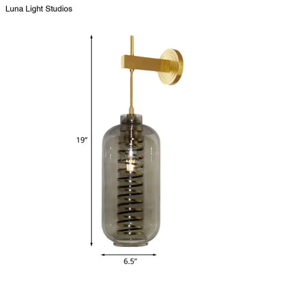 Post-modern brass wall sconce with smoke gray glass cylinder and coiled black spiral design for bedroom lighting