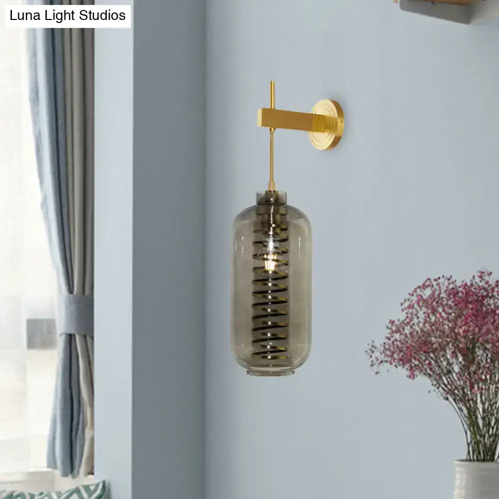 Post-modern brass wall-mounted sconce with a smoke gray glass cylinder and amber spiral design for bedroom lighting
