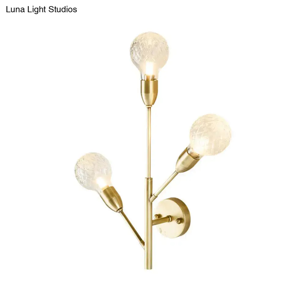 Gold-toned post-modern brass wall light fixture with three clear lattice glass textured bulbs for bedroom use