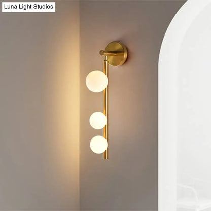Post modern gold finish wall lamp with three frosted glass globe bulbs arranged vertically on a slender rod