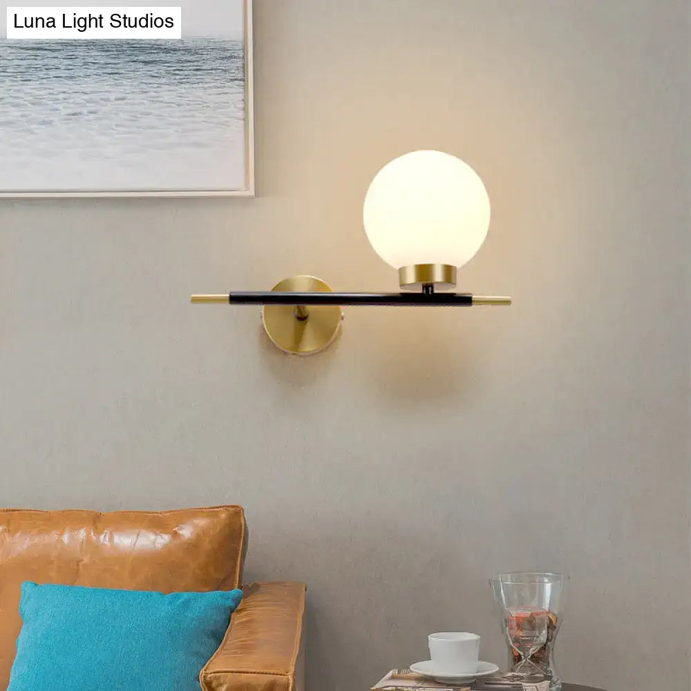 Modern sphere wall sconce with frosted glass globe, brass accents, and black metal arm for bedroom lighting