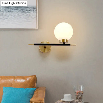 Modern sphere wall sconce with frosted glass globe, brass accents, and black metal arm for bedroom lighting