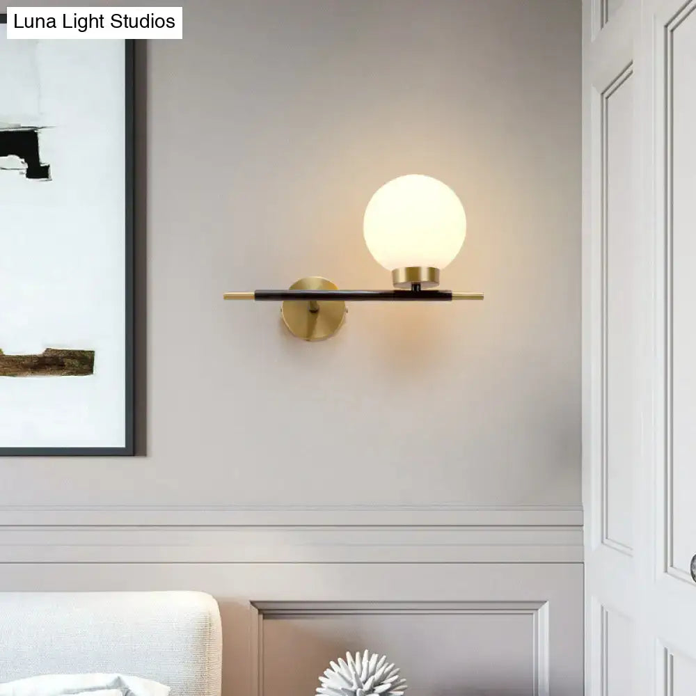 Post-modern white and brass sphere wall sconce with frosted glass globe and brass-finished metal base for bedroom light