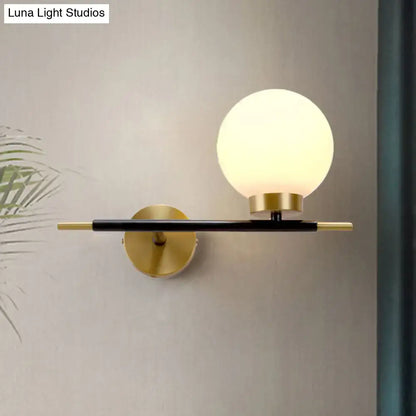 Post-modern white and brass sphere wall sconce with frosted glass globe and black metal arm for bedroom lighting