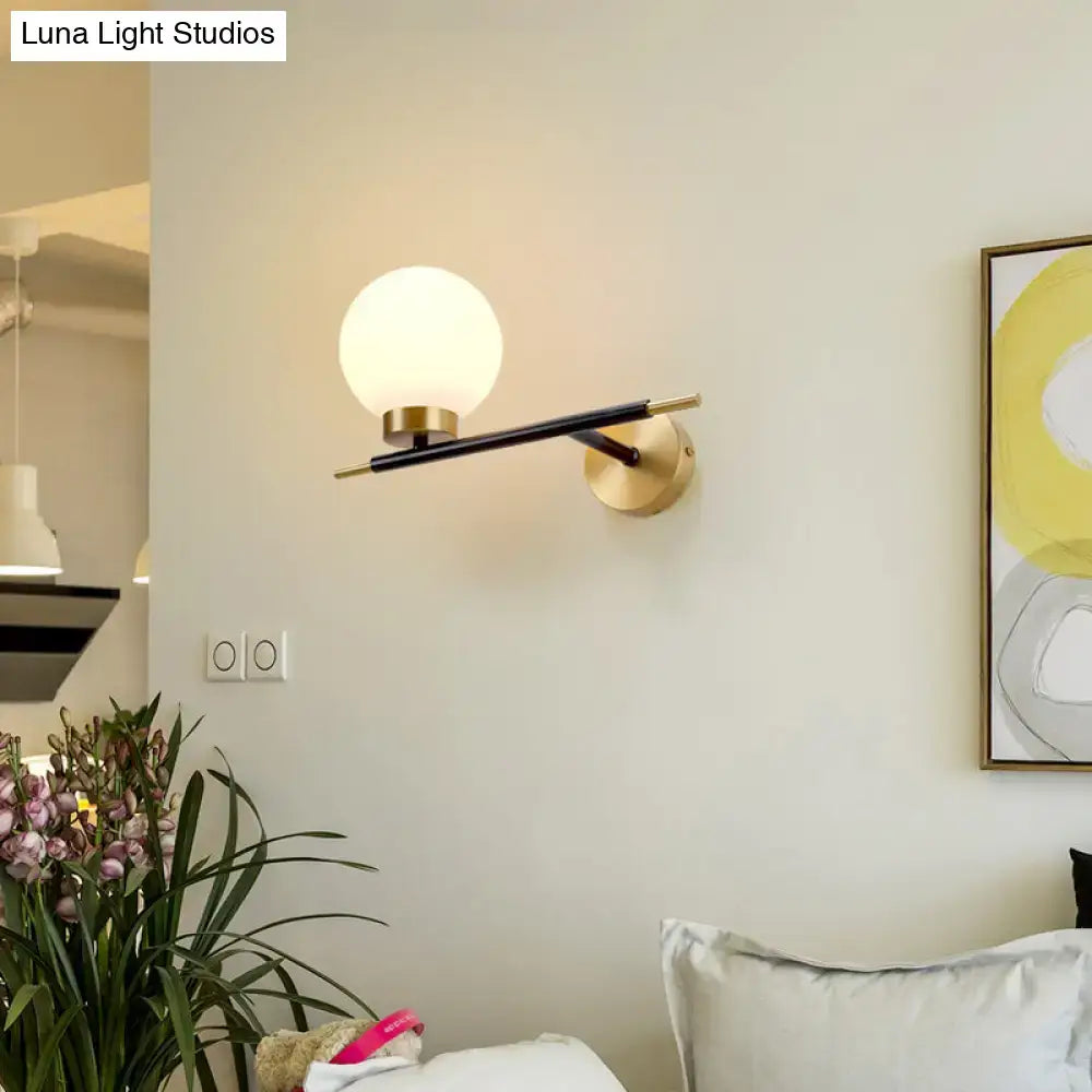 Post-modern sphere wall sconce with matte black arm, gold brass mount, and frosted glass globe for bedroom light