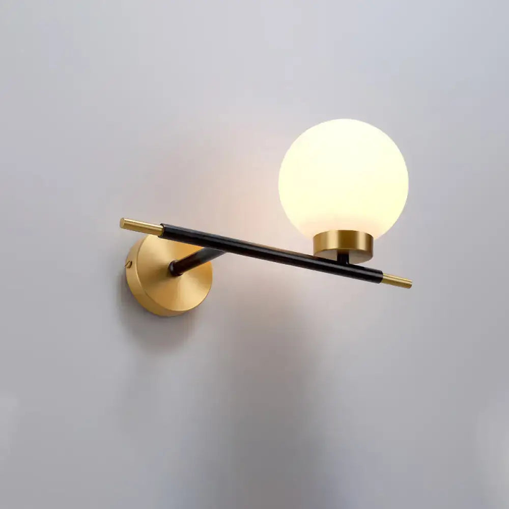 Post-modern sphere wall sconce with matte black arm, gold-toned accents, and frosted glass globe for bedroom lighting