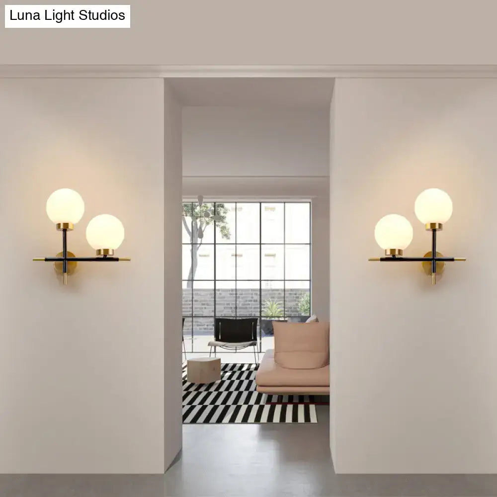 Post-modern white and brass sphere wall sconce with frosted glass globe shades on black and gold metal frame for bedroom lighting