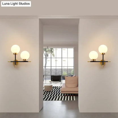 Post-modern white and brass sphere wall sconce with frosted glass globe shades on black and gold metal frame for bedroom lighting
