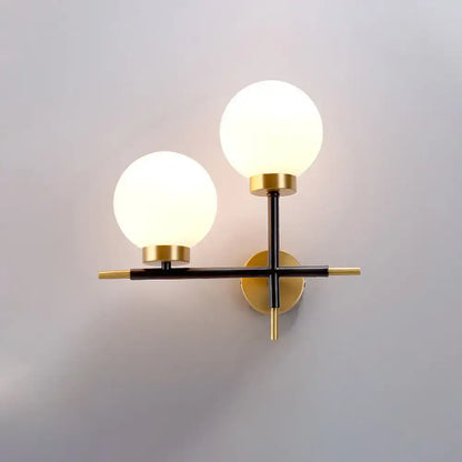 Modern two-light sphere wall sconce with frosted glass globes and brass and black metal frame for bedroom lighting