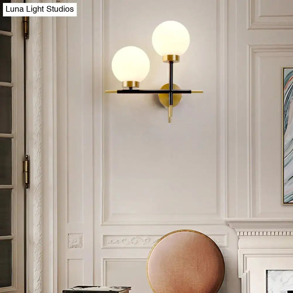 Modern post-modern white and brass sphere wall sconce with frosted glass globes and black metal frame for bedroom lighting