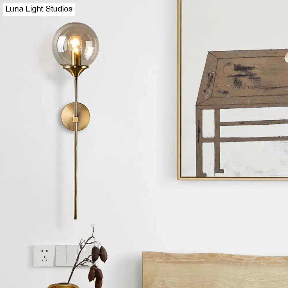 Brass-finished wall sconce with smoke grey spherical glass globe housing an exposed e27 bulb for bedroom use