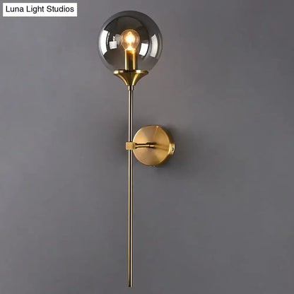 A sleek brass postmodern wall sconce with smoke grey glass and an exposed e27 bulb for bedroom use