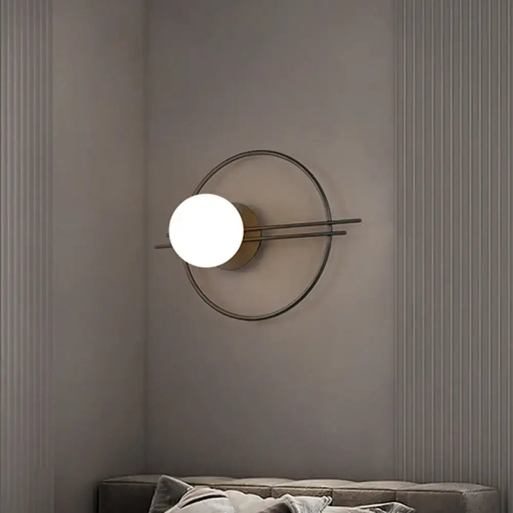 Modern minimalist sconce light with black brass circular frame and glowing white glass bulb for bedroom use