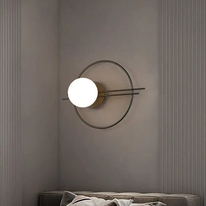 Modern minimalist sconce light with black brass circular frame and glowing white glass bulb for bedroom use
