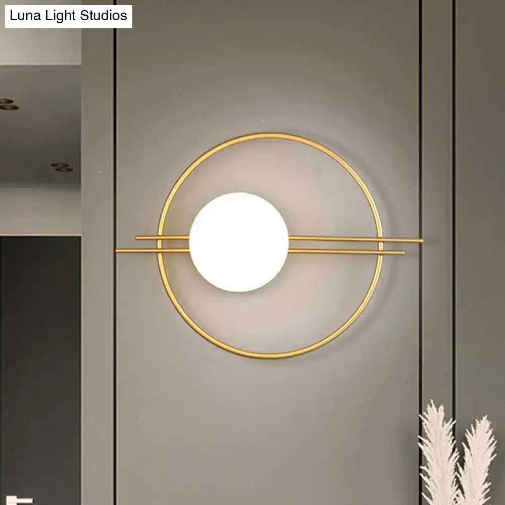 Modern gold-toned circular sconce light with white glass globe and black brass intersecting horizontal bars for bedroom use