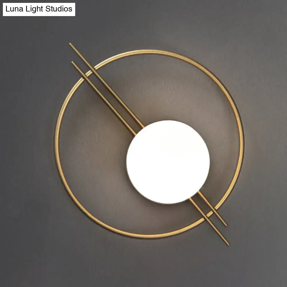 Modern gold-toned circular sconce light with black brass intersecting lines and white glass illuminated disc for bedroom use