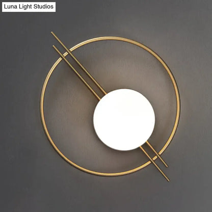 Modern gold-toned circular sconce light with black brass intersecting lines and white glass illuminated disc for bedroom use