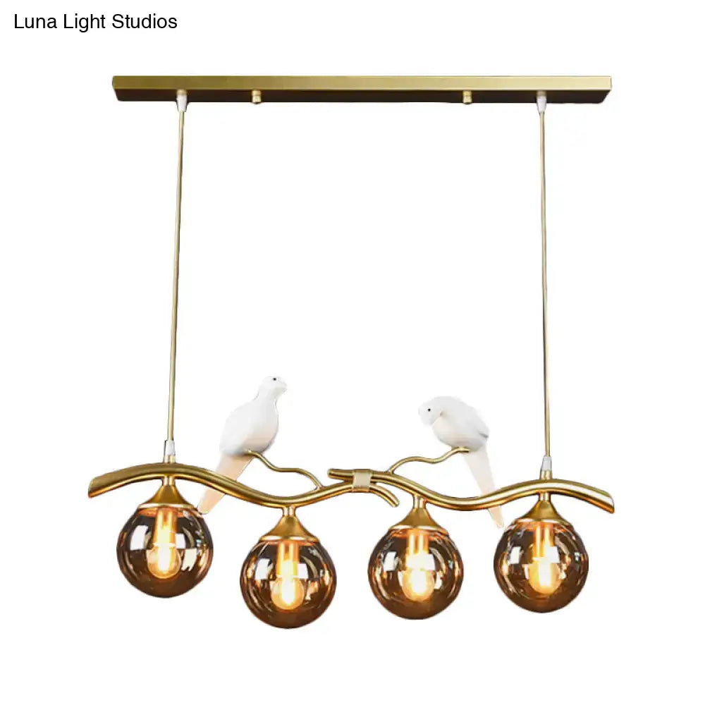 Gold-toned black gold pendant light with amber ball glass shades and white ceramic bird decor on iron frame