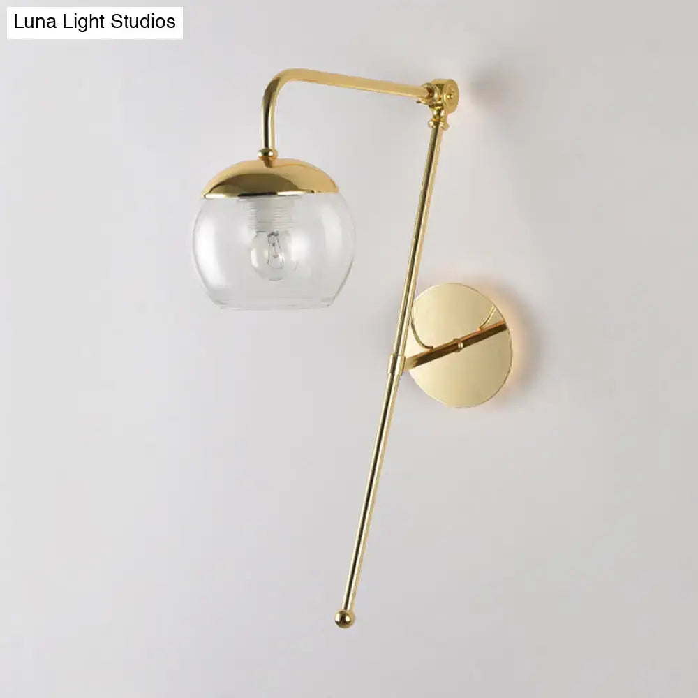 Gold-finished swing arm wall sconce with clear glass globe and brass accents for postmodern bedroom lighting