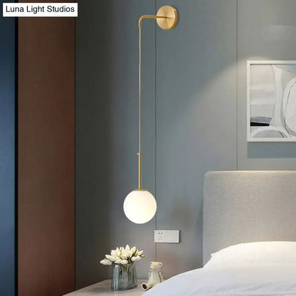 Gold-toned wall lamp with slender curved arm and frosted glass globe for bedroom in postmodern style